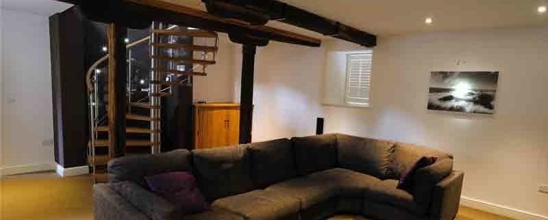 large living room with big black sofa Infront of spiral staircase