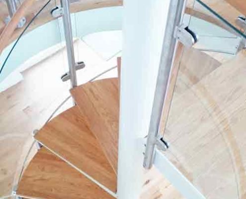 looking down on oak steps of a modern spiral stair with curved glass panels