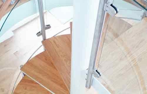 looking down on oak steps of a modern spiral stair with curved glass panels