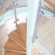 looking down on oak steps of a modern spiral stair with curved glass panels