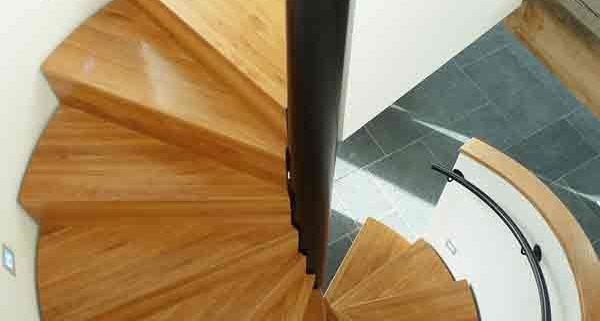 looking down on the oak steps of a spiral staircase with black wall mounted handrail
