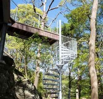 galvanised outdoor spiral stair leading up to a wooden walkway in a woodland setting