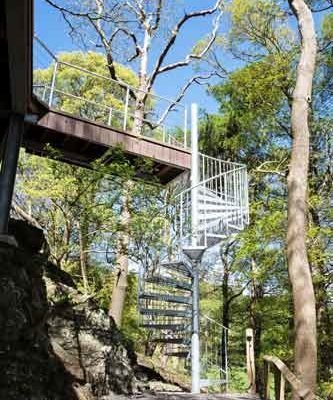 galvanised outdoor spiral stair leading up to a wooden walkway in a woodland setting