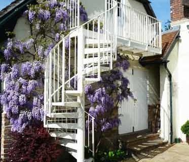 white outdoor spiral staircase with balcony with purple flowers