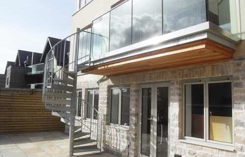 suspended balcony with frameless glass balustrade and a galvanised spiral staircase