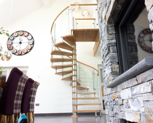 stainless and glass spiral staircase behind a dry stone wall