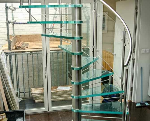 spiral stair in a house with glass steps above a dark tiled floor