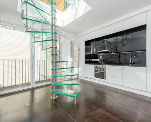 Green glass spiral staircase in a kitchen with a black cooker and white walls