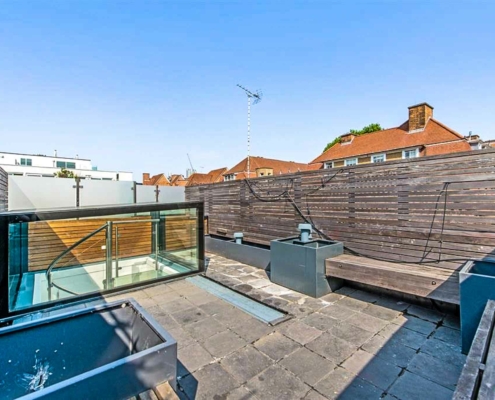 Roof terrace with blue sky above and patio slabs to terrace. Spiral stair in background below a glass hatch