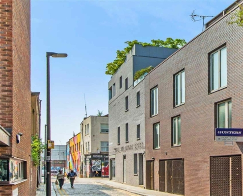 Street view of shoreditch with square buildings either side, blue sky and two people walking