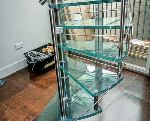 view from side of spiral stair with glass steps in a house with timber floor