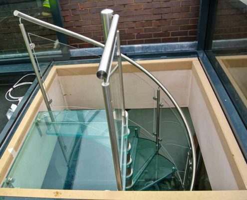 Looking down on the top of a glass step spiral stair. Large square opening and square glass platform