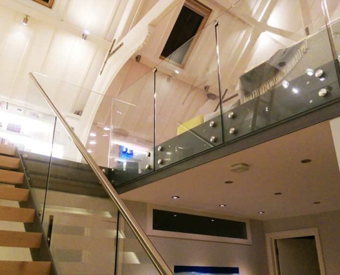 modern staircase with open risers and frameless glass balustrade around opening of stairwell. White ceiling beyond