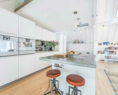 Modern white kitchen with granite worksurface. Glass balustrade to right