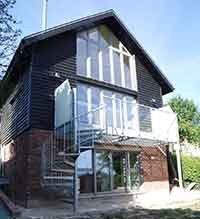 external picture of a house with black cladding and a spiral staircase and balcony in foreground