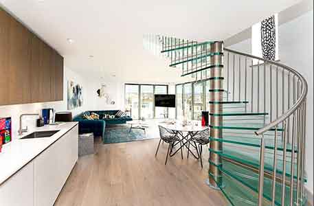 kitchen with timber floor and glass spiral stair with living room beyond