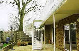 garden picture with a tree and a white spiral stair leading to a walkway