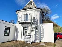 white building with blue sky behind and a spiral staircase in front