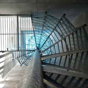 view from below looking through the perforated steps of a spiral stair to a blue light above the shaft