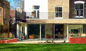external picture of the rear of a house with green grass and a black spiral staircase