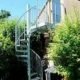outdoor spiral stair with bushes to the left and right. Garage to rear of shot