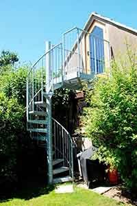outdoor spiral stair with bushes to the left and right. Garage to rear of shot