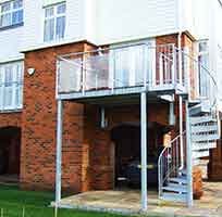 outdoor steel balcony on a red brick house with a spiral stair leading up