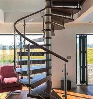 wooden spiral stair with glass panels and dark timber handrail. huge window behind