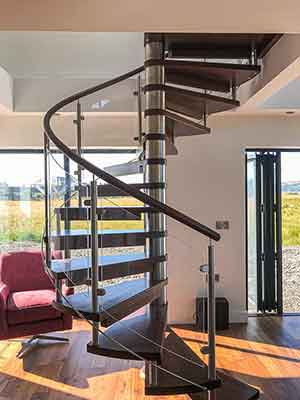 wooden spiral stair with glass panels and dark timber handrail. huge window behind