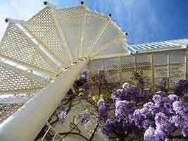 view looking up at the steps of an outdoor spiral stair in white. Blue sky behind