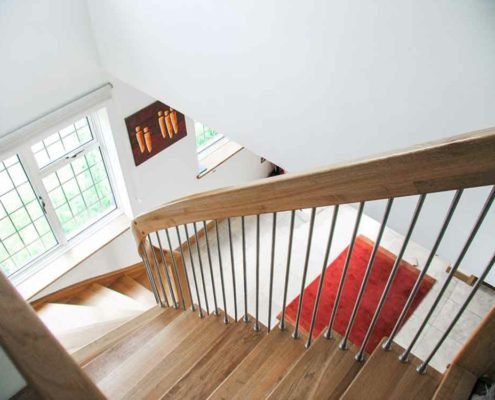 looking down an oak staircase with red rug below