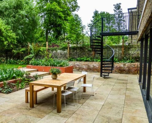 table and chairs outside in a garden with spiral stair behind