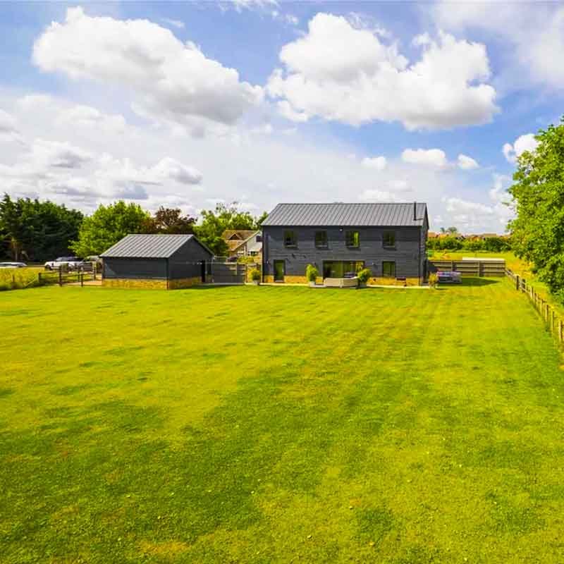 Large-grass-area-behind-dark-grey-house-with-blue-sky-above