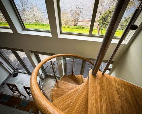 looking down on a wooden spiral staircase and windows behind with a lake beyond